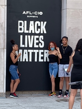 2 Black women, 1 Black man in front of AFL-CIO Black Lives Matter poster